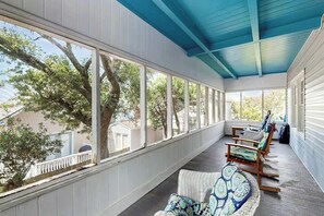 A covered porch with large windows, wicker furniture, and a view of trees and a house. - Williams Beach Bunker B (North Myrtle Beach)