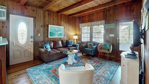 A wooden-paneled room with a brown leather sofa, a blue armchair, a white armchair, a glass coffee table, and a patterned rug. - Williams Beach Bunker B (North Myrtle Beach)