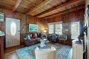 A wooden-paneled room with a brown leather sofa, a blue armchair, a white armchair, a glass coffee table, and a patterned rug. - Williams Beach Bunker B (North Myrtle Beach)