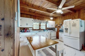 A kitchen with wooden walls, white cabinets, a wooden table, and a ceiling fan. - Williams Beach Bunker B (North Myrtle Beach)
