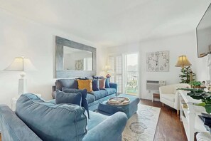 Un salon moderne avec un canapé bleu, un fauteuil blanc et une table basse. Un grand miroir est placé au-dessus du canapé et une horloge est accrochée au mur.