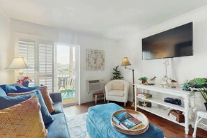 Ein Wohnzimmer mit einer Couch, einem Couchtisch mit Büchern, einem Fernseher und einem weißen Sessel.