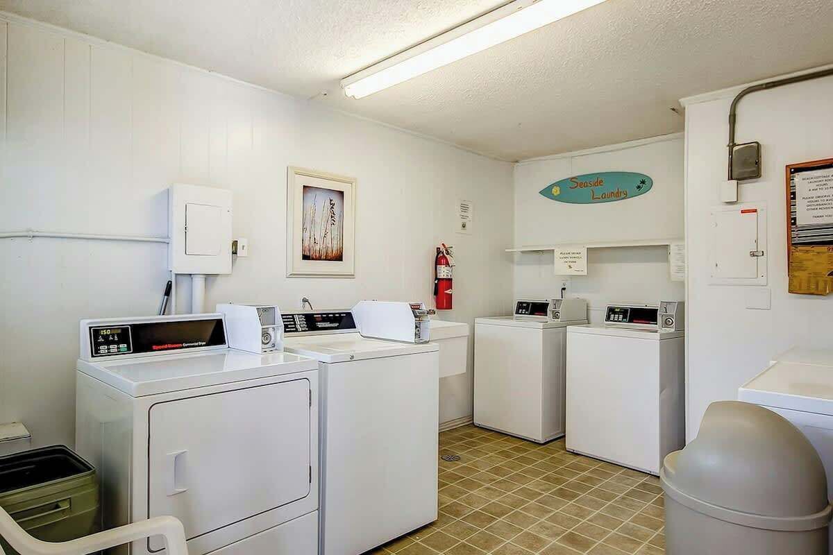 A laundry room with two washing machines, a dryer, a trash can, and a fire extinguisher.
