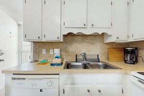 A kitchen with white cabinets, a double sink, a coffee maker, and a dishwasher. - Beach Cottages at OD - 11B (North Myrtle Beach)