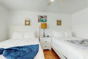 A hotel room with two beds, a nightstand with a lamp, and wall decorations including framed shells and a mermaid painting. - Beach Cottages at OD - 11B (North Myrtle Beach)