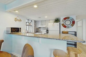 A modern kitchen with a central island, bar stools, and a decorative clock on the wall. - Arcadian Dunes 12-245 (Myrtle Beach)