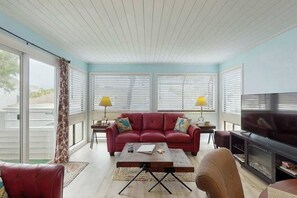 A living room with a red sofa, a coffee table, a television, and a fireplace. - Arcadian Dunes 12-245 (Myrtle Beach)