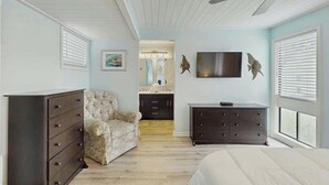 Ein Schlafzimmer mit einem Bett, einem Schminktisch, einem Sessel, einem Fernseher und einem Deckenventilator.