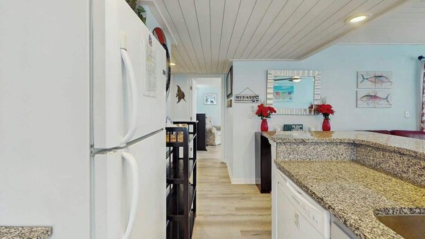 Eine moderne Küche mit einem weißen Kühlschrank, einer Granitarbeitsplatte und Holzdielen.