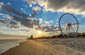 Une plage avec une grande grande roue, des vagues et un coucher de soleil.