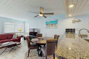 Un salon moderne comprenant un coin repas, un ventilateur de plafond, un téléviseur et une cuisine équipée d’un four à micro-ondes.