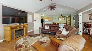 A spacious living room with a large flat-screen TV, a ceiling fan, a brown leather sofa, and a wooden entertainment center. - Sterling Pointe 113-F at Wachesaw III (Murrells Inlet)