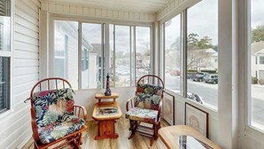 A sunroom with large windows, two wicker chairs with floral upholstery, and a small wooden table with a decorative item. - Sterling Pointe 113-F at Wachesaw III (Murrells Inlet)