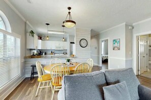 Une cuisine moderne avec des meubles blancs, un coin repas avec des chaises en bois et un canapé gris.