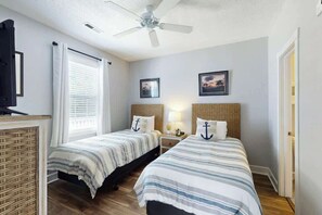 Une chambre avec deux lits, un ventilateur de plafond, une télévision et une fenêtre avec des rideaux.
