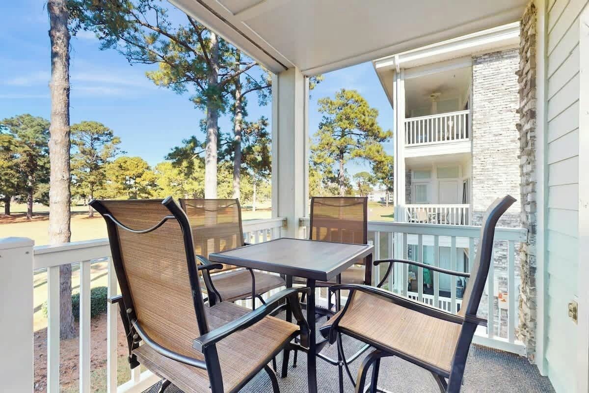 An outdoor patio with a table and chairs, a white railing, and a view of trees and a building.