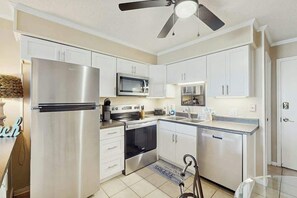 A modern kitchen with stainless steel appliances, white cabinetry, and a ceiling fan. - A Place at the Beach IV - 235 (Myrtle Beach)