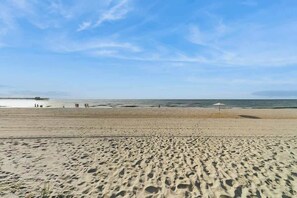 En sandstrand med fotspår, en pir i fjärran och en klar himmel.