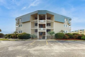 A multi-story building with a central entrance, balconies, and a parking lot in front. - A Place at the Beach IV - 235 (Myrtle Beach)