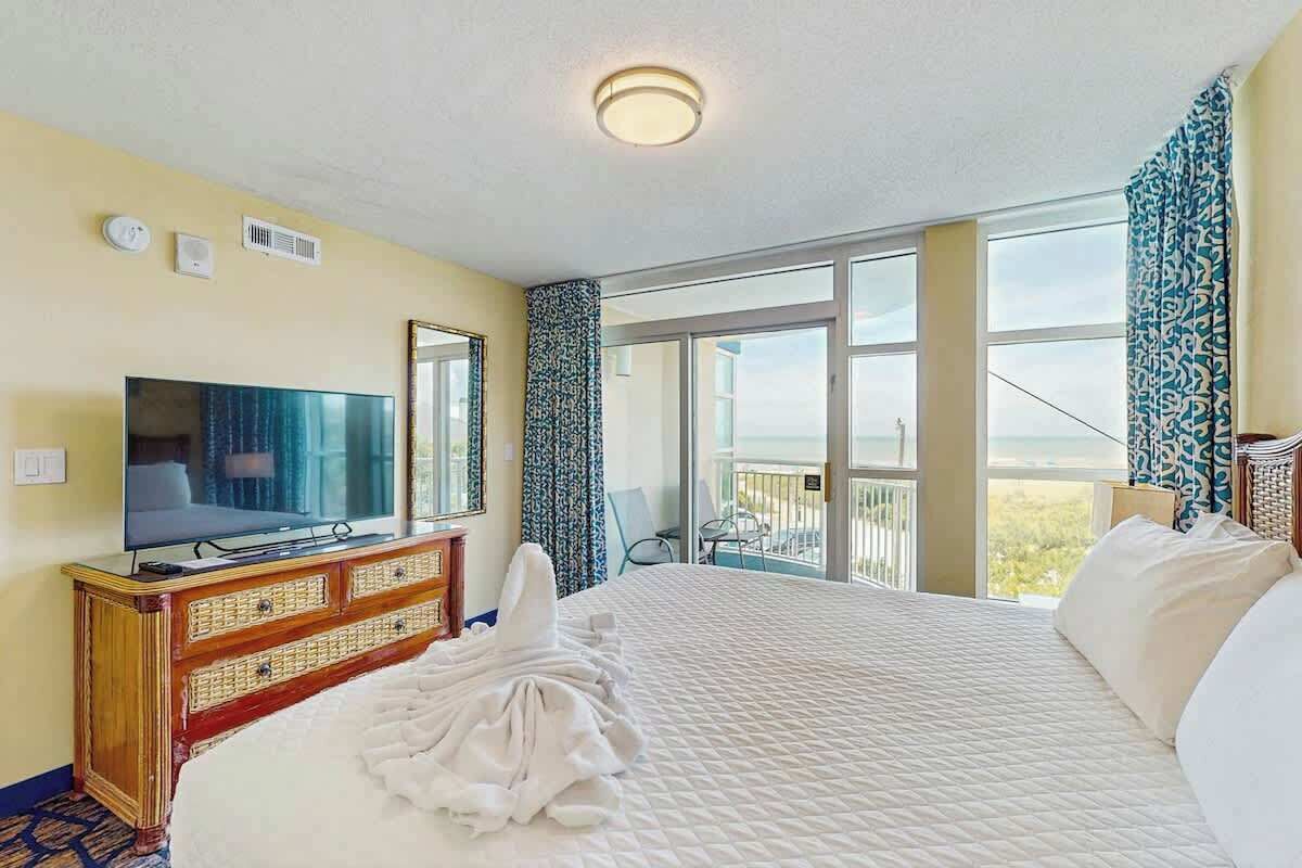 A hotel room with a large bed, a television, a dresser, and a balcony with a view.