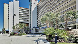 A multi-story hotel with a parking garage, palm trees, and a clear sky. - Beachfront Bliss Retreat (Myrtle Beach)