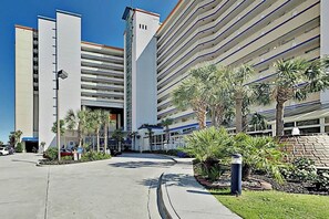 A multi-story hotel with a parking garage, palm trees, and a clear sky. - Beachfront Bliss Retreat (Myrtle Beach)