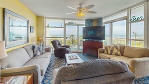 A spacious living room with a large television, comfortable seating, and a balcony with a view. - Beachfront Bliss Retreat (Myrtle Beach)