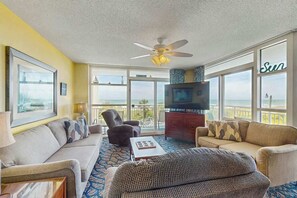 A spacious living room with a large television, comfortable seating, and a balcony with a view. - Beachfront Bliss Retreat (Myrtle Beach)