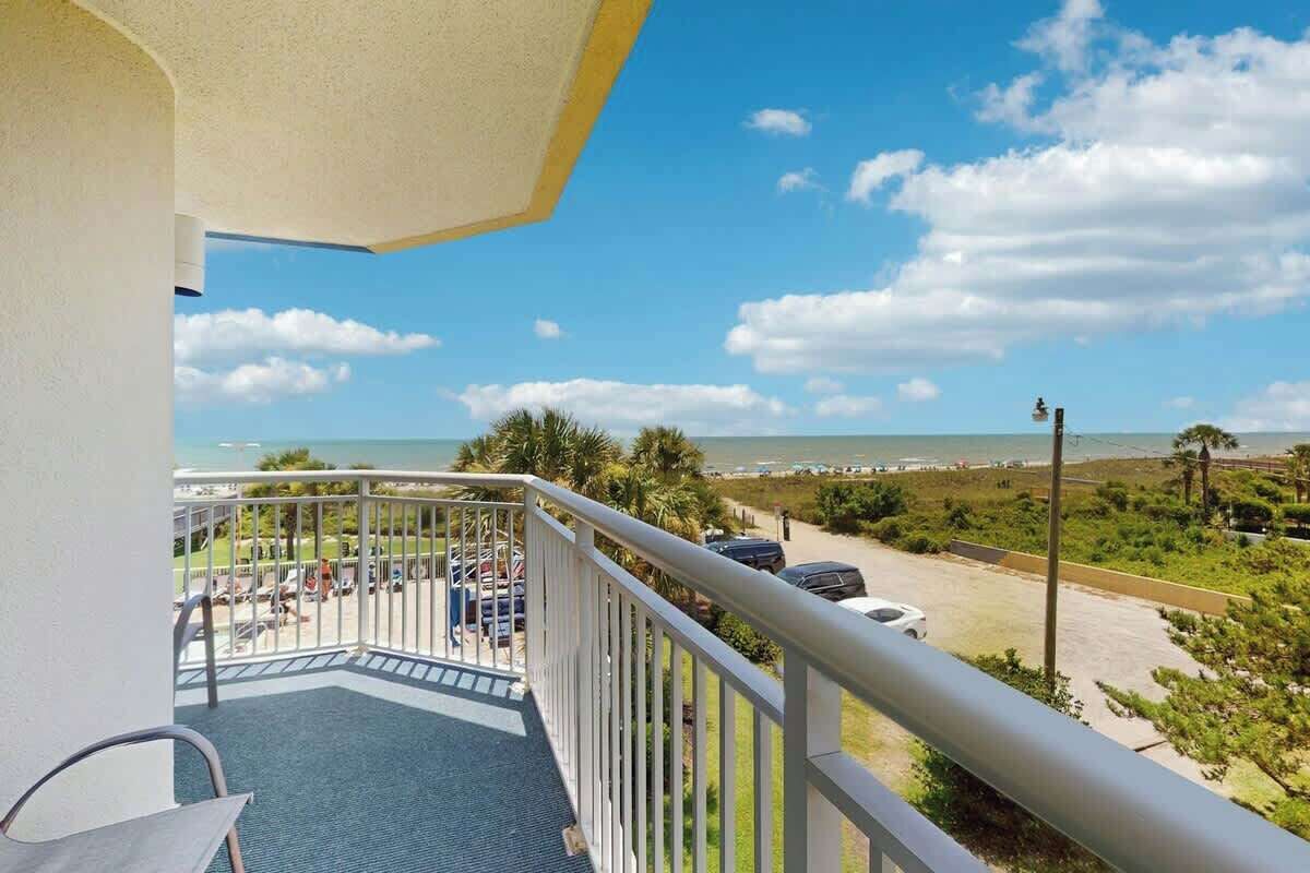 En balkon med hav- og strandudsigt, en parkeringsplads og en klar himmel.