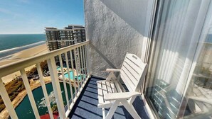 Een balkon met een witte stoel, een zwembad en uitzicht op zee en gebouwen.