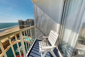 A balcony with a white chair, a pool, and a view of the ocean and buildings. - Sea Watch Unit 1605 Condo (Myrtle Beach)
