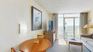 Een hotelkamer met een ronde houten tafel, een bank, een televisie en een balkon met uitzicht.