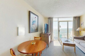 A hotel room with a round wooden table, a sofa, a television, and a balcony with a view. - Sea Watch Unit 1605 Condo (Myrtle Beach)