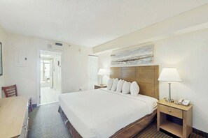 A hotel room with a large bed, bedside tables with lamps, a door leading to a hallway, and a painting on the wall. - Sea Watch Unit 1605 Condo (Myrtle Beach)