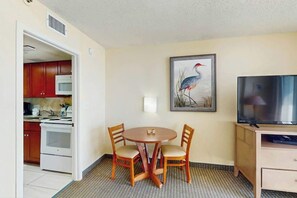 A compact room with a dining table, two chairs, a television, and a kitchen area visible through an open doorway. - Sea Watch Unit 1605 Condo (Myrtle Beach)