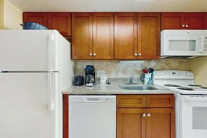 A compact kitchen with wooden cabinets, a white refrigerator, a microwave, a coffee maker, and a dishwasher. - Sea Watch Unit 1605 Condo (Myrtle Beach)