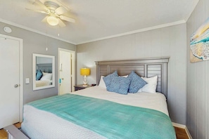A bedroom with a bed, a ceiling fan, a nightstand, and a wall-mounted lamp. - A Place at the Beach VI - 105 (Myrtle Beach)