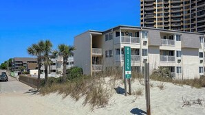 A beachfront building with balconies, a sign indicating the name 'MAISON 21', and a clear blue sky. - A Place at the Beach VI - 105 (Myrtle Beach)