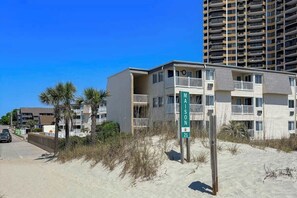 Ein Gebäude direkt am Strand mit Balkonen, einem Schild mit dem Namen 'MAISON 21' und blauem Himmel.