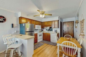 A compact kitchen with wooden cabinets, a refrigerator, microwave, and a dining area with chairs and a table. - A Place at the Beach VI - 105 (Myrtle Beach)