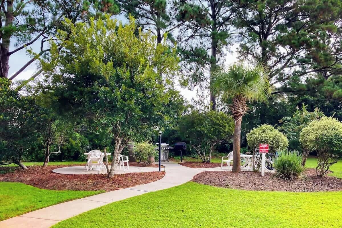 A landscaped outdoor area with a paved walkway, seating areas, and various trees.
