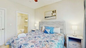 Una camera da letto con un letto, comodini, una ventola a soffitto, un quadro e una porta che conduce al bagno.