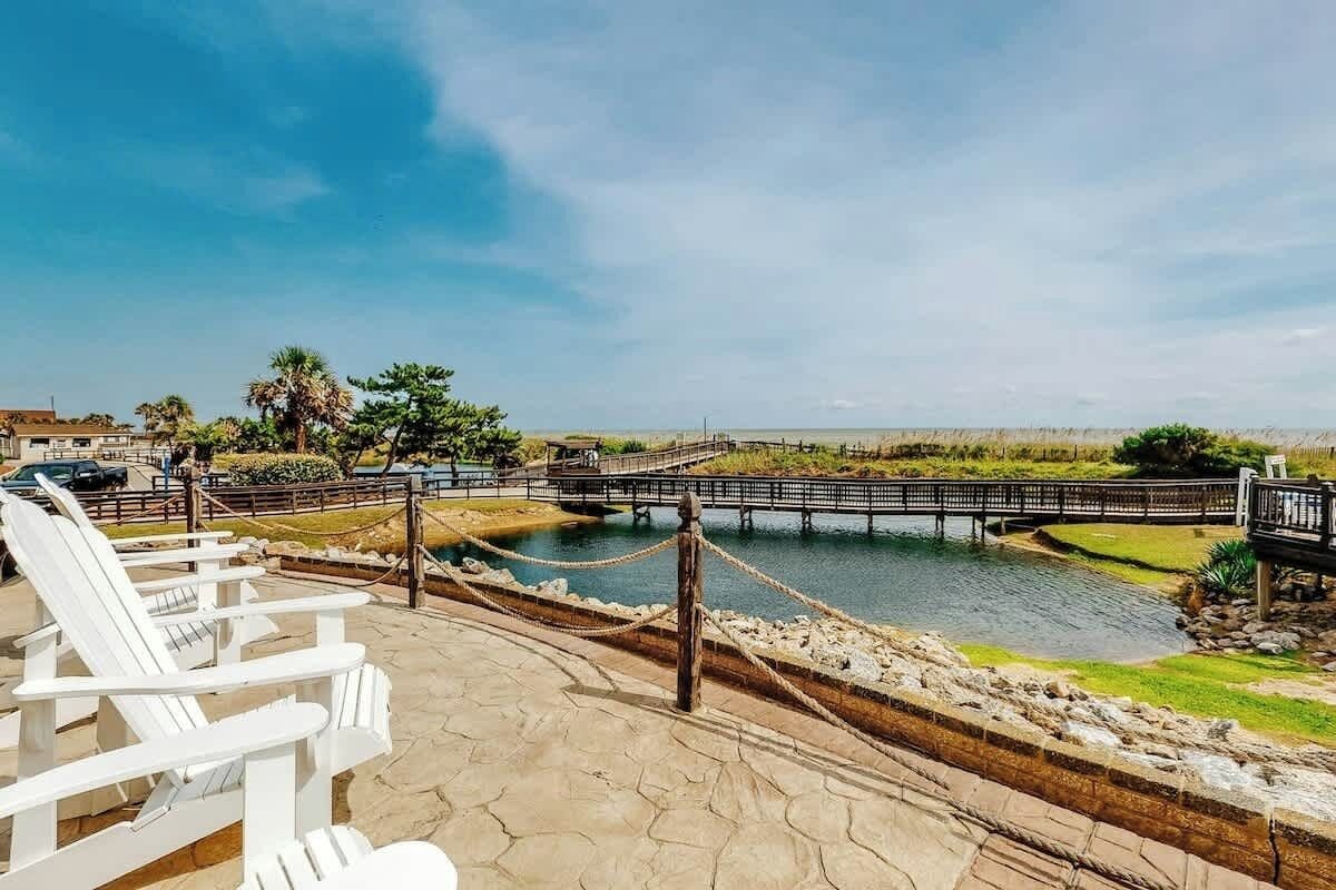 A waterfront view with a wooden dock, lounge chairs, and a clear sky.