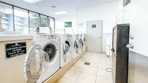 Un lavadero con varias lavadoras, una puerta cerrada y un cartel que indica los horarios de cierre.