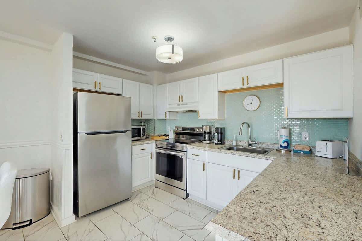 A modern kitchen with white cabinets, stainless steel appliances, a granite countertop, and a clock on the wall.