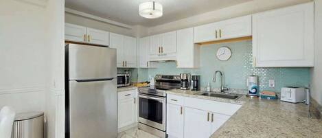 A modern kitchen with white cabinets, stainless steel appliances, a granite countertop, and a clock on the wall.