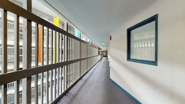 Un pasillo con barandilla, una ventana de marco azul y una puerta con un letrero rojo.