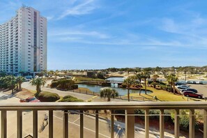 A high-rise building with a view of a landscaped area including a pond, palm trees, and parked cars. - Myrtle Beach Resort 344B (Myrtle Beach)