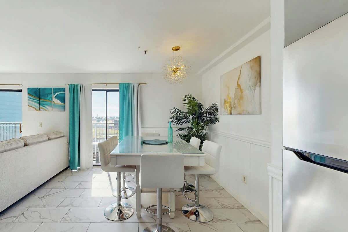 A modern dining area with a glass table, white chairs, and a view of the sea.