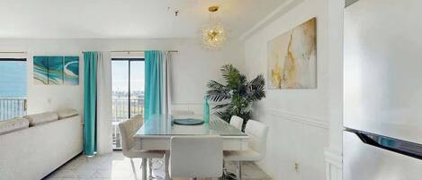 A modern dining area with a glass table, white chairs, and a view of the sea.